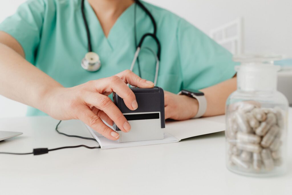 Medical Operations Lead/RIP 2 Closeup of a doctor stamping a prescription with a bottle of pills on a desk.